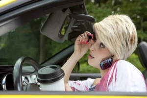 Distracted driver putting on makeup, talking on phone with a drink cup in hand